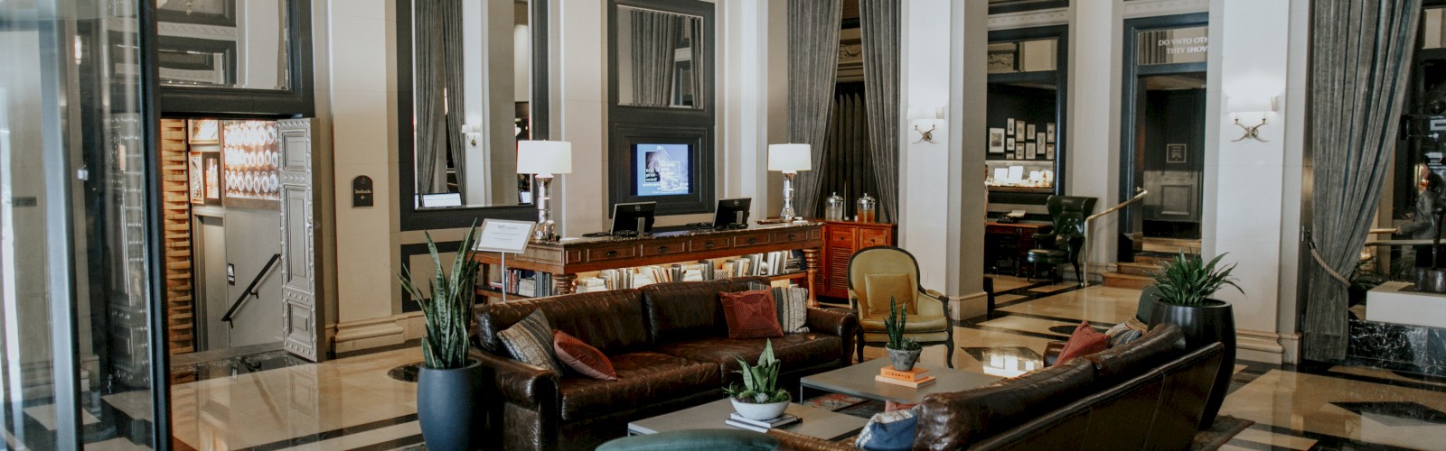 The image shows a spacious, elegant lobby with luxurious seating, modern decor, large mirrors, and a blend of classic and contemporary design elements.