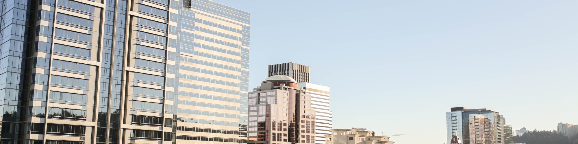 The image shows a cityscape with several modern skyscrapers and buildings under a clear blue sky.