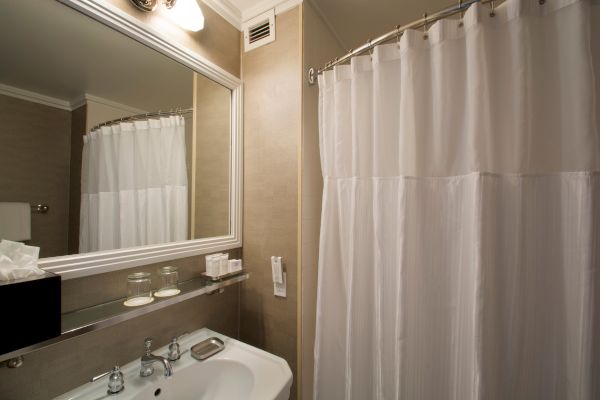 A bathroom with a sink, a mirror with lights, a shelf with glasses and toiletries, and a shower curtain covering the bathtub or shower area.