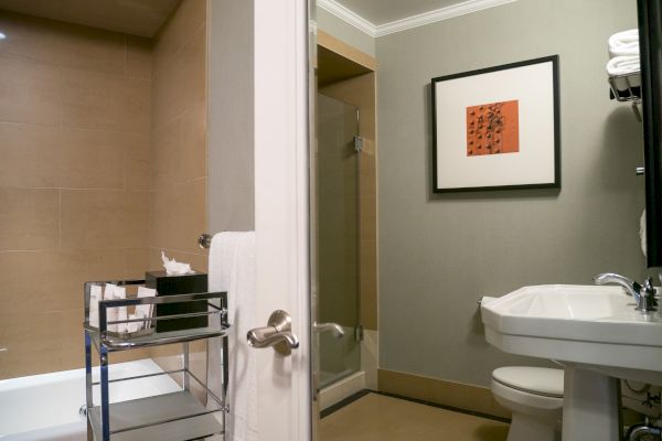 The image depicts a bathroom with a bathtub, a sink, a toilet, and a shower area. Towel rack and framed picture on wall are visible.