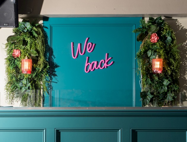 The image shows a teal wall with pink neon text 