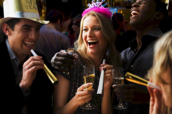 A group of people celebrating at a party, wearing hats and holding drinks, appear to be enjoying New Year's festivities.