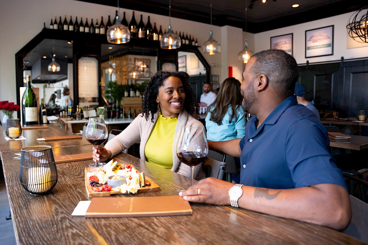 A couple enjoys wine and a cheese platter at a cozy restaurant, engaging in conversation and smiling at each other.