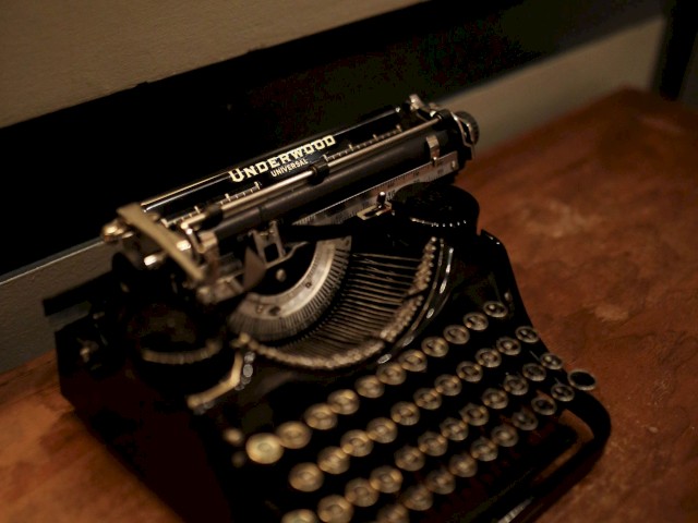 The image shows a vintage typewriter placed on a wooden desk, shot in low lighting, creating a nostalgic ambiance.