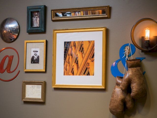 A wall gallery features framed photos, artwork, boxing gloves, a light fixture, an @ symbol, and decorative items.