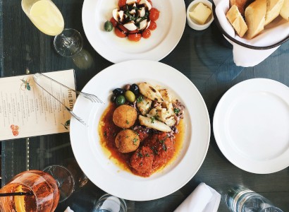 A table set with plates of food, including a main dish, a salad, bread, drinks, and cutlery, viewed from above.