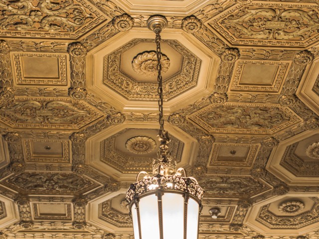 An ornate ceiling with intricate patterns and a large hanging lantern-style light fixture. The ceiling has hexagonal designs and detailed moldings.