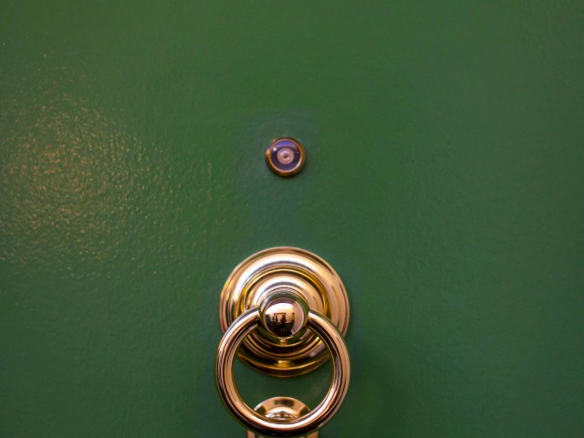 This image shows a green door with a brass door knocker and a peephole above it.