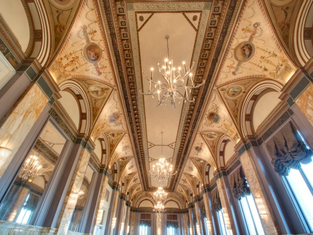 This image shows an ornate, classical interior with high ceilings, chandeliers, and intricate paintings and decorations on the ceiling and walls.