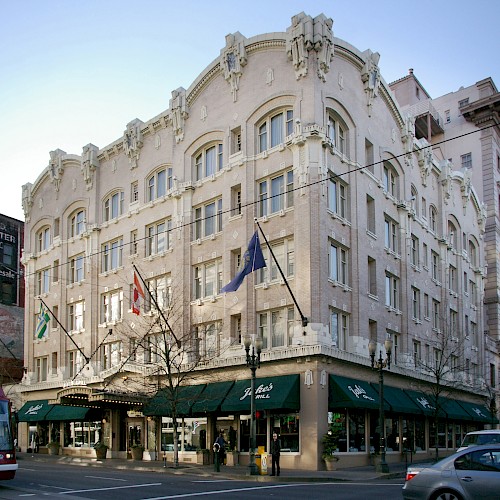 The image shows a historic, multi-story building with ornate architecture, flags, and a streetcar nearby. It's located on a busy urban corner.