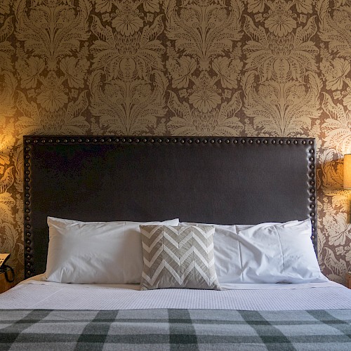 Bridgetown Parlor Suite - A cozy bedroom with a large bed, patterned wallpaper, bedside lamps, and wooden nightstands, creating a warm and inviting atmosphere.