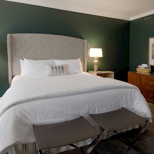 Terrace Studio Suite - This image shows a hotel room with a large bed, lamps on side tables, and artwork above a wooden dresser.