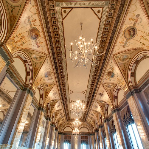 An ornate, high-ceilinged room with decorative arches, chandeliers, and intricate artwork on the ceiling.