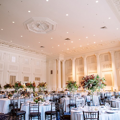 An elegant banquet hall with high ceilings, decorated tables, and floral centerpieces, ready for a formal event or wedding reception.