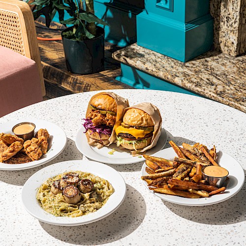 The image shows a table with dishes: burgers with toppings, a plate of fried food, a pasta dish with mushrooms, and fries with dip.