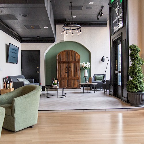 A stylish modern interior with green chairs, a wooden door feature, shelves with bottles, and a chandelier.