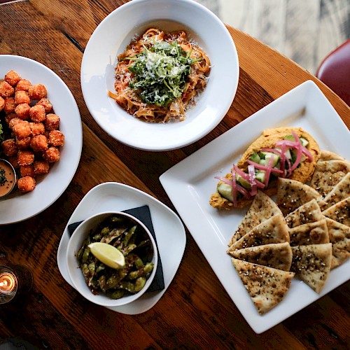 The image shows a table with dishes including a burger with fries, pasta, a side dish with a lemon wedge, and flatbread with toppings.