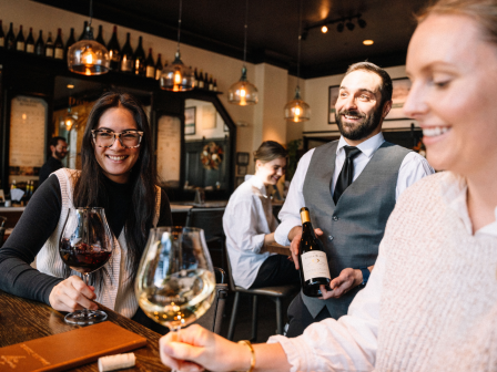 People enjoying wine in a cozy restaurant setting, with a waiter serving a bottle.