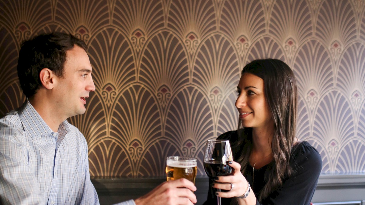 A couple is toasting with drinks at a restaurant table, enjoying a meal together in a cozy setting.