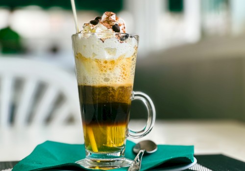 This image shows a layered coffee drink topped with whipped cream and chocolate chips, served in a glass on a saucer with a spoon.