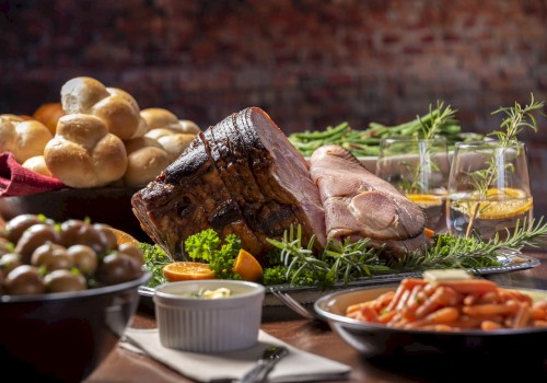 A sumptuous feast featuring roasted meat, carrots, potatoes, bread rolls, garnishes, and beverages, elegantly arranged on a table.