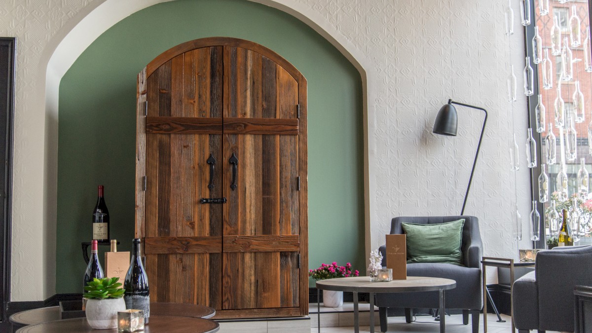 A cozy room with a wooden door, modern chairs, tables with decor, and a large window with a city view completes the scene.