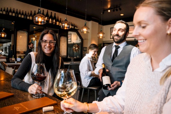 People enjoying wine at a cozy bar, with a waiter serving a bottle.