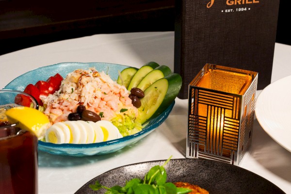 A table with a seafood and salad dish, a drink, and a menu from Jake's Grill. A lit candle adds ambiance.