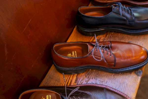 A row of polished leather shoes is lined up on a wooden bench, each featuring different shades of brown and black finishes.