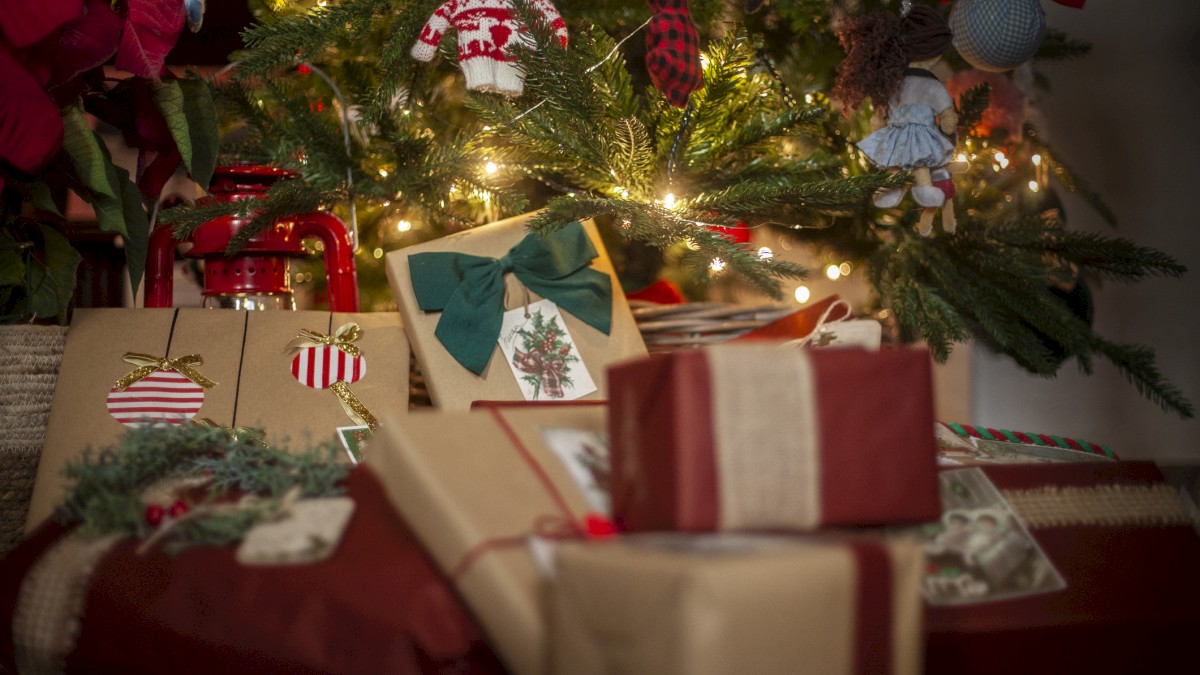 A decorated Christmas tree with twinkling lights and wrapped gifts in festive brown and red paper under it.
