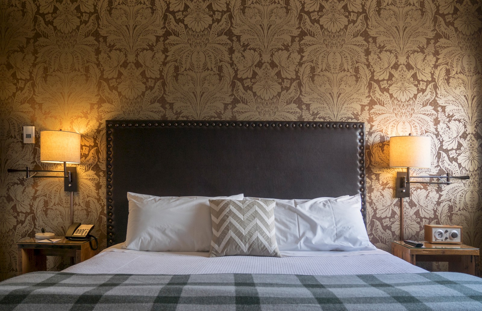 A neatly made bed with pillows, lamps on bedside tables, and decorative wallpaper in a cozy bedroom setting.