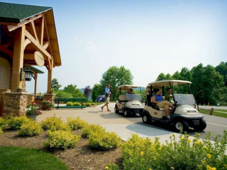 The image shows people near a golf course, with two golf carts and a clubhouse surrounded by greenery and yellow flowers.