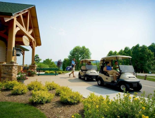 Two golf carts with people parked near a building surrounded by greenery and yellow flowers, with one person walking toward the building.