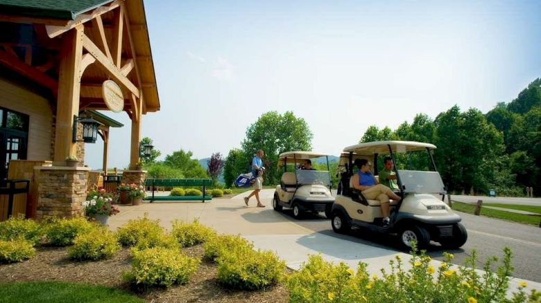 The image shows a golf course entrance with two golf carts and a person carrying a golf bag. There are lush greenery and a wooden structure.
